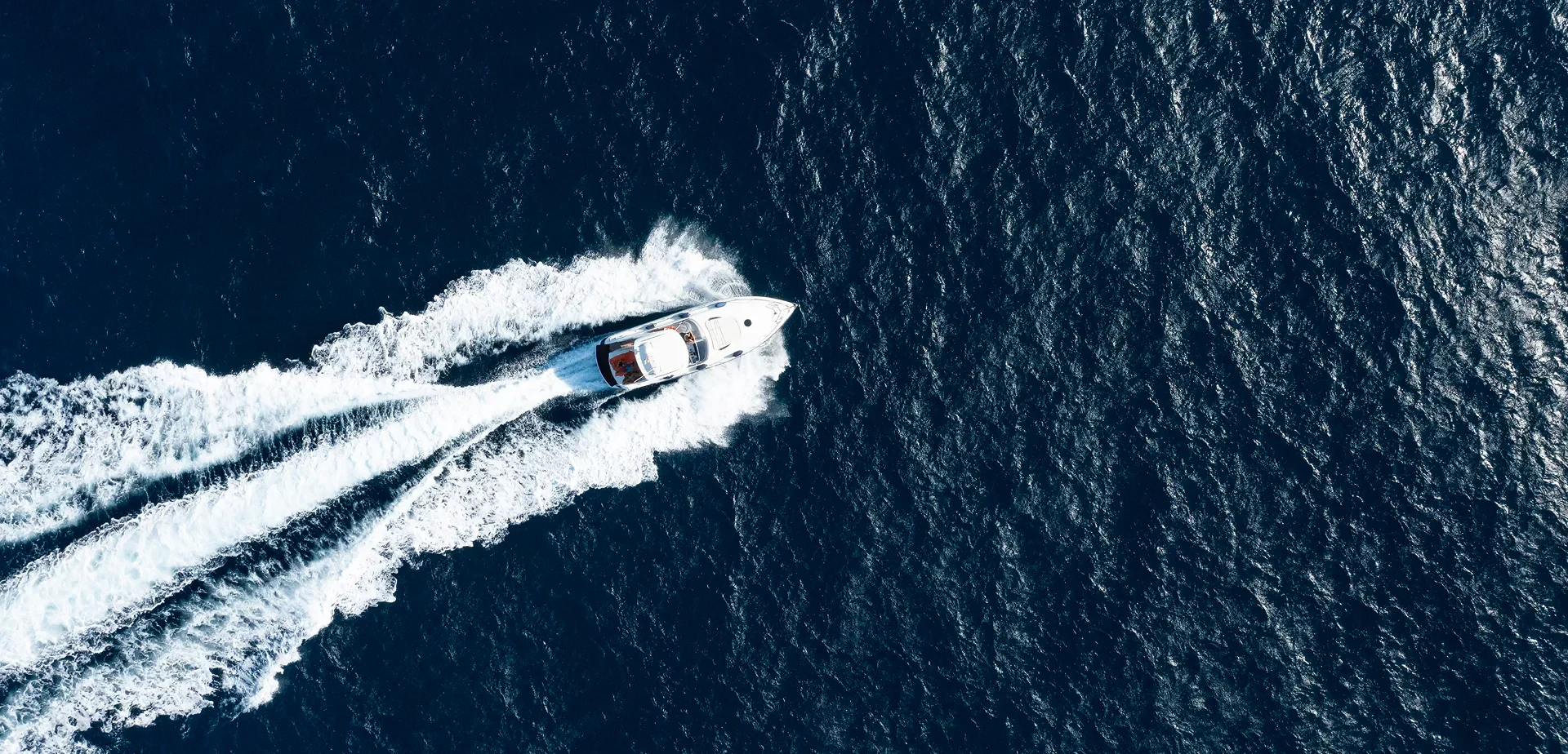 A white motorboat on a dark blue sea, leaving a long white wake behind it