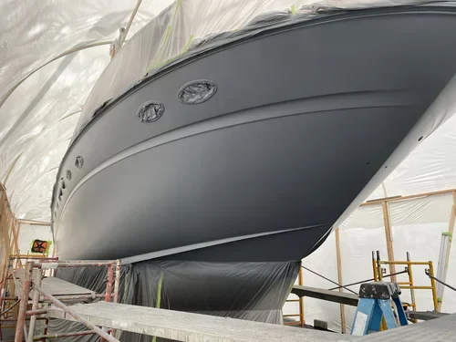 A large yacht undergoing painting or refinishing inside a service facility, surrounded by scaffolding