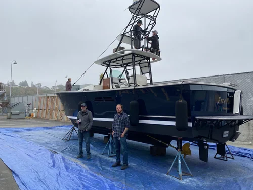 A large, dark-hulled center console boat on land with two men standing in front of it