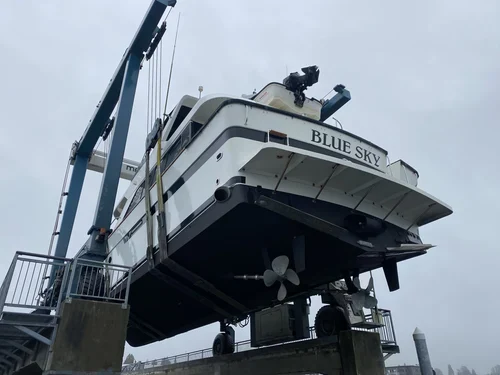 A boat named 'Blue Sky' is being lifted out of the water by a large crane at a marina