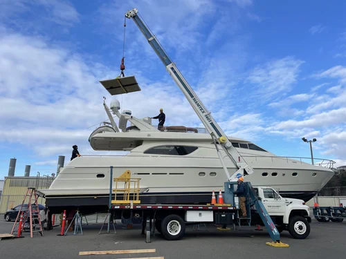 A crane lifts a large yacht onto a flatbed truck