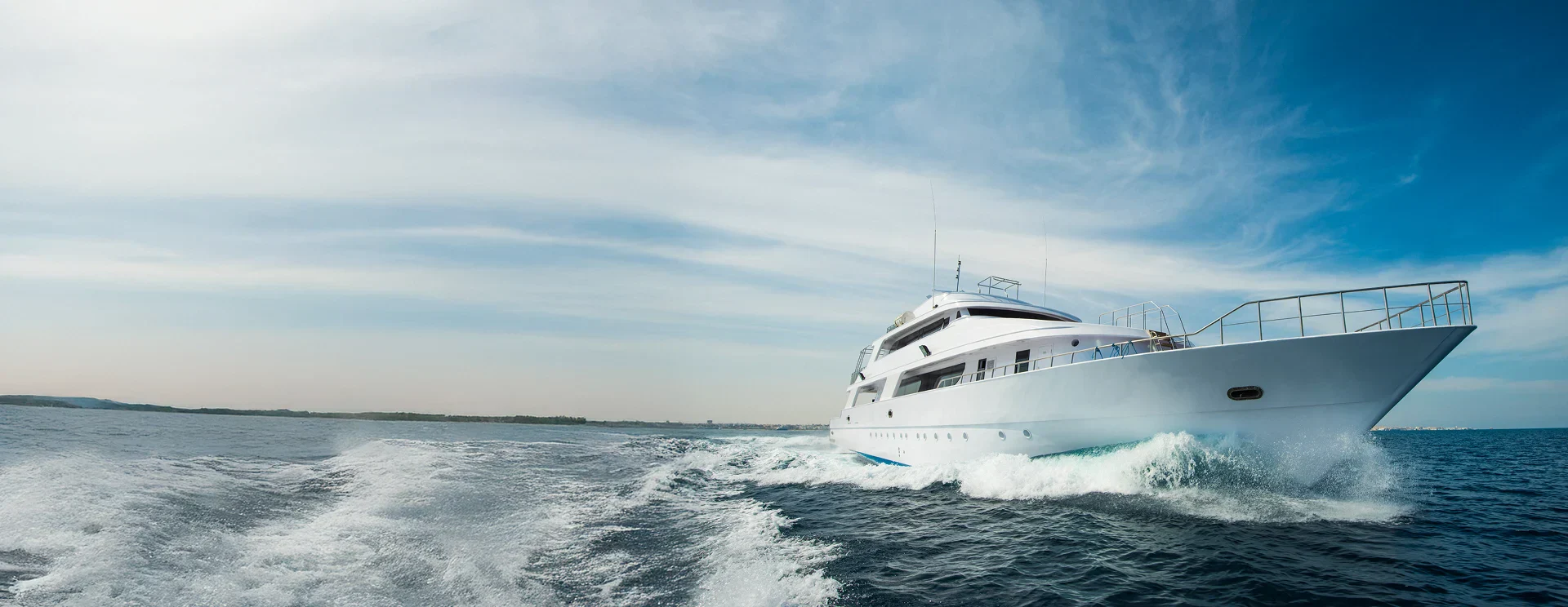 A large white yacht moving quickly through the blue ocean, creating a wake behind it