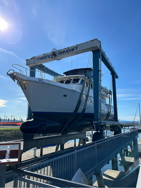 A large white boat is being lifted out of the water by a Marine Travelift