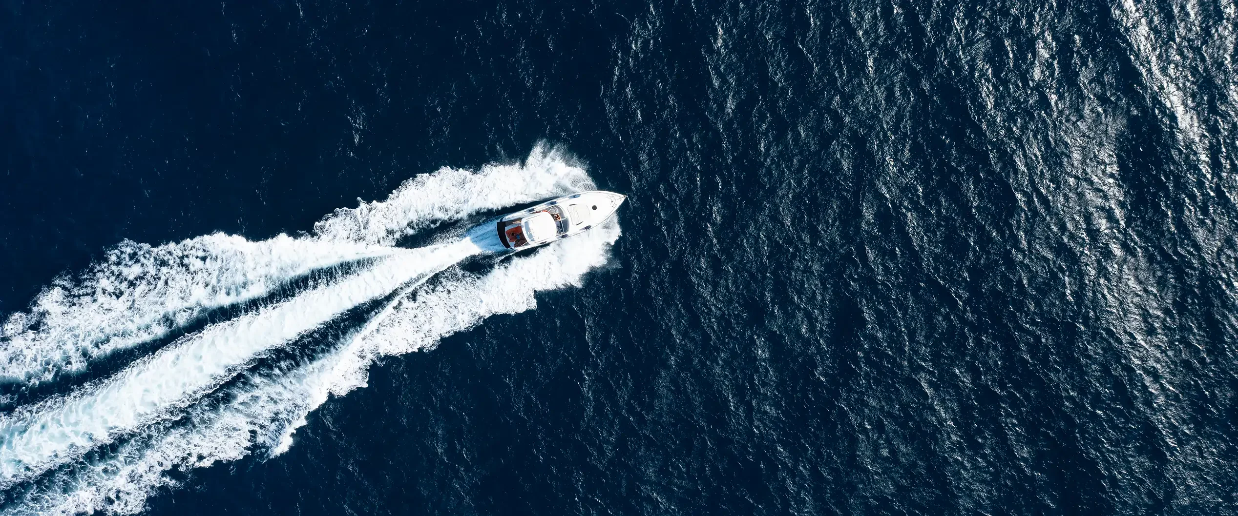 A white motorboat on a dark blue sea, leaving a long white wake behind it